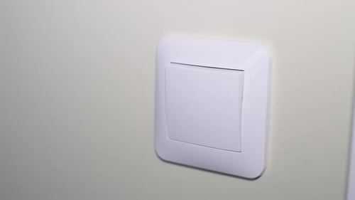 Closeup de um interruptor de luz na parede sendo ligado pela mão de uma mulher