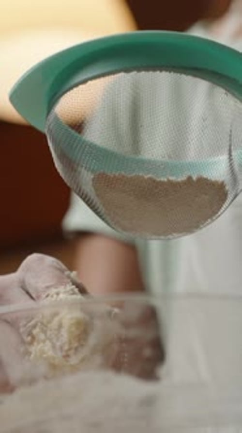 Vertical video. Person Sifting Flour into a Bowl with Dough, Adding Final Ingredients for Perfect Co