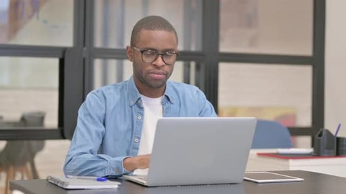 African Businessman Looking at Camera while Working on Laptop in Office