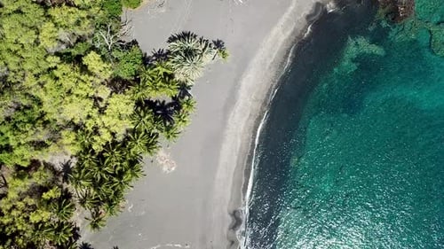 aerial of crystal blue water off lava rock black sand beach on big island hawaii