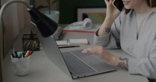 Young Woman Works, Talks on Phone at Laptop