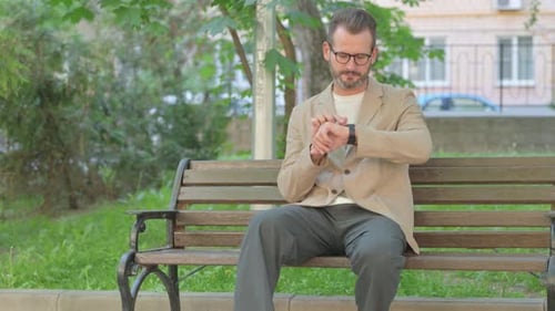 Man Checking Smart Watch While Sitting on Bench