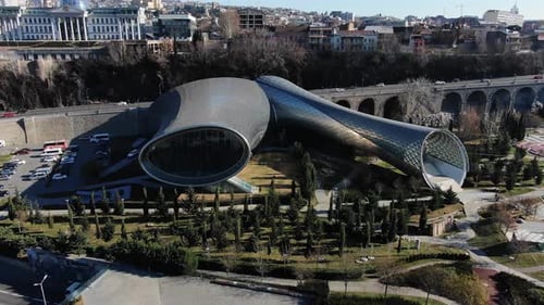 Camera is Panning Over a Park Featuring the Modern Architecture of the Bridge of Peace in Tbilisi