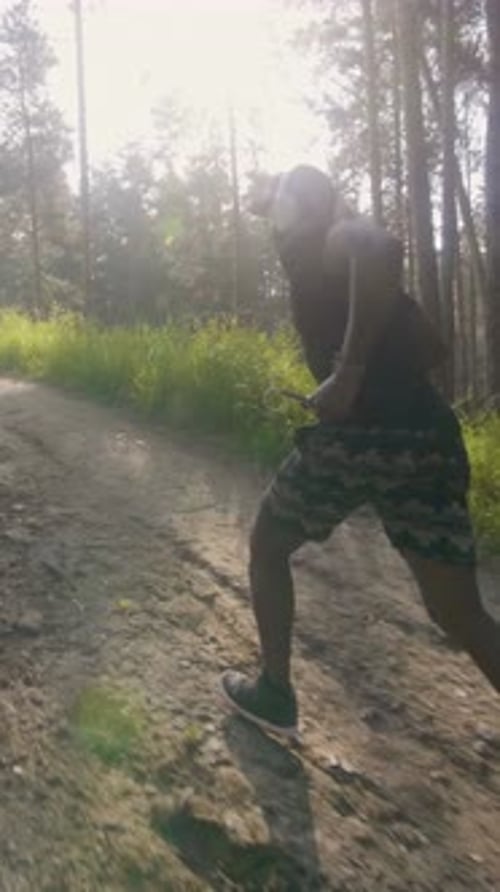 Athletic Individual Running on a Dirt Path Surrounded By Lush Greenery and Sunlight Filtering