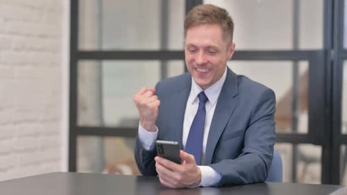 Young Businessman Celebrating Success on Phone in Office