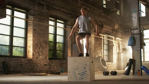 Muscular Fit Man Energetically Box Jumps in Hardcore Gym doing Part of Cross Fitness Training Progr