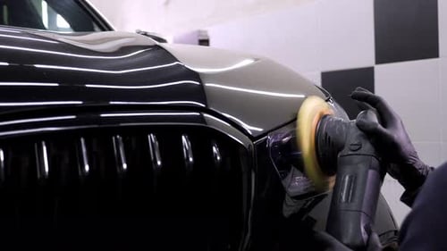A Man Polishes a Black Car with a Car Polishing Machine at a Car Dealership