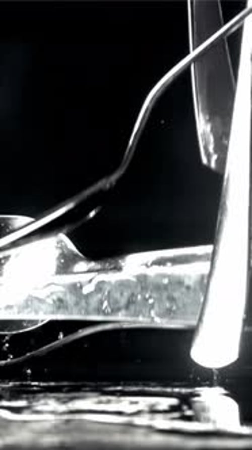 Cutlery cae sobre una mesa negra mojada filmada con una cámara de alta velocidad a 1000 fps