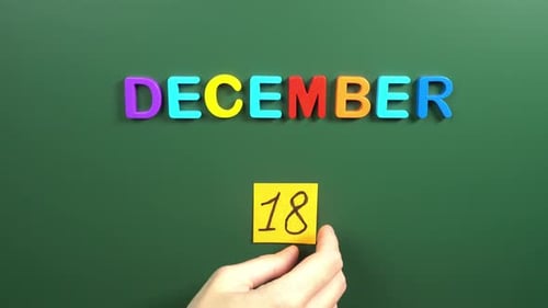 Hand sticking a sticker 18 December calendar day on school board. 18 date of December. Eighteenth
