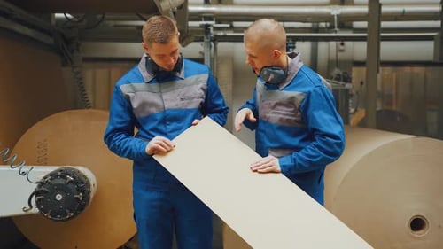 Zwei männliche Arbeiter oder Ingenieure aus der Kartonfabrik diskutieren über die Qualität von Karton im Vergleich zu
