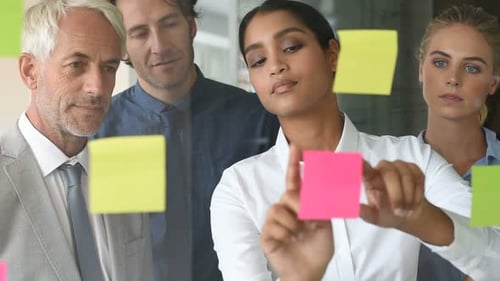 Multi Ethnic Young Businesswoman Sticking Adhesive Notes on Glass Wall in Office