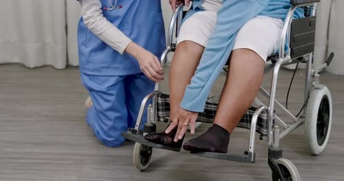 Closeup view of nurse adjusting footrest for elderly male cancer survivor in wheelchair after