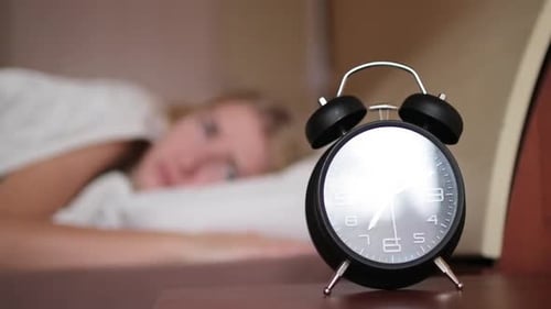 Schlafendes Mädchen, das vom Weckruf aufwacht und ihn ausschaltet, klassisches Klingeln der Uhr