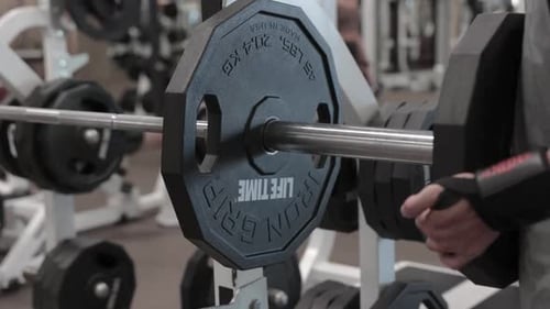 man placing weight plate on bench press in gym