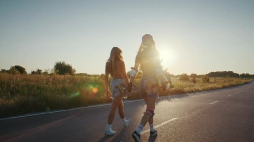 Sporty Women Walk on Country Road at Sunset Carrying Surfskates