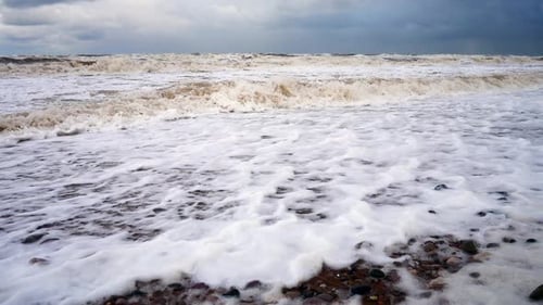 Powerful stormy rolling coastal ocean waves foam blowing in rough windy weather low angle