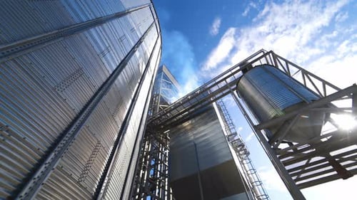 Silver grain elevator in sunny weather. Metal construction of a large industrial plant.