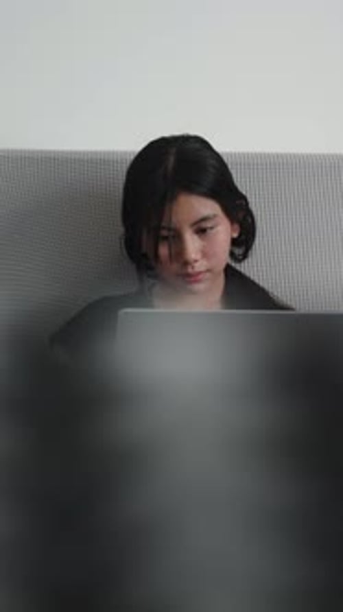 Focused Young Woman Working Remotely From Home Using Laptop in Bed