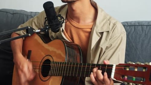 Man plays acoustic guitar with microphone in home