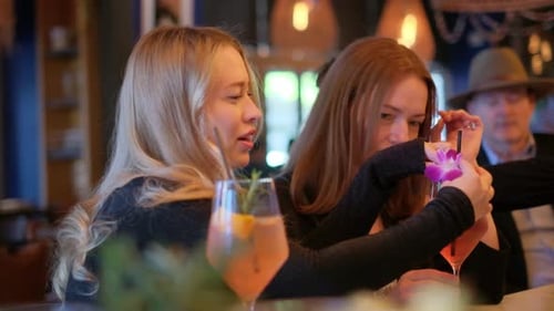 Two Friends Enjoy Cocktails at a Restaurant Sharing Laughs and Selfies