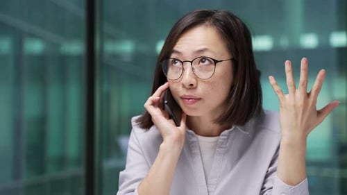 Angry asian businesswoman arguing talking on mobile phone at workplace in office. Frustrated female