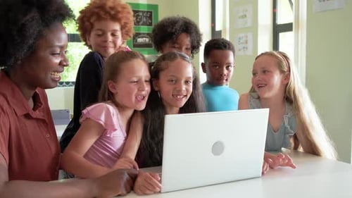 Diverse students, African American teacher in rust blouse pointing at laptop, watching and laughing