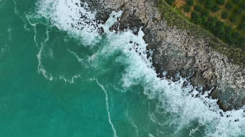Aerial Video of Ocean Waters Hitting Coastal Cliffside With Sea Foam and Turquoise Surface Below