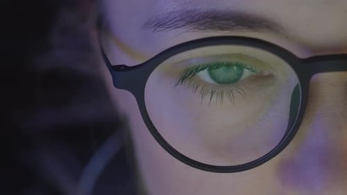 Close-up woman eyes in glasses looking on the monitor and and working with charts and analytics