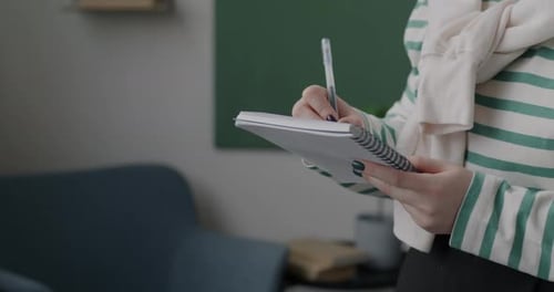 Closeup of Hands Writing in Notebook While Businesswoman Standing in Office