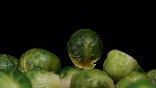 Mountains of Brussels sprouts rotating on a black background, slowly emerging from darkness