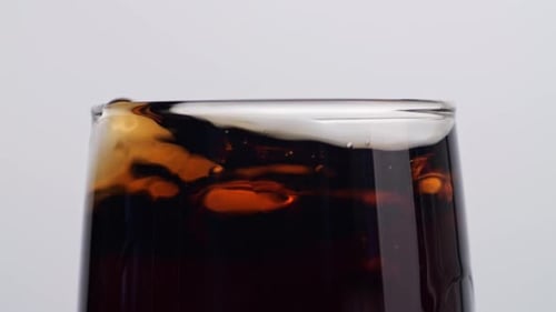Nahaufnahme von Eiswürfeln, die in ein Glas frischer Cola auf weißem Hintergrund fallen