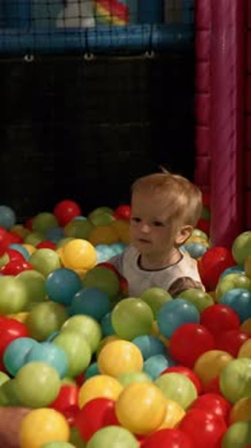Vertical of Mom Throws Colorful Balls Playing with Little Son in Pool