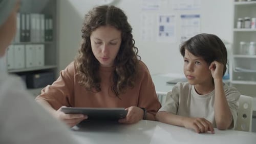 Woman with Child Reviewing Medical Documents and Speaking with Doctor in Clinic