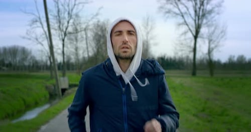 A Young nice green eyes man running in a small road into the wild nature and looking straight to t