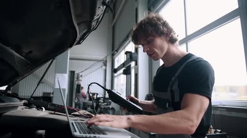 Computerdiagnose von Autos, junger Mechanikerspezialist, männlich, verwendet Laptop-Technologie bei der Reparatur