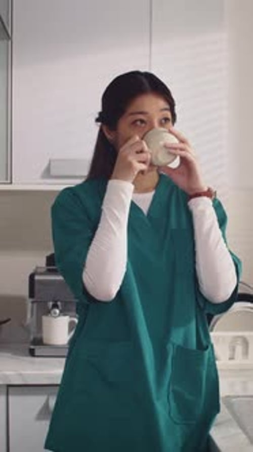 Woman in Scrubs Drinking Tea in Bright Kitchen