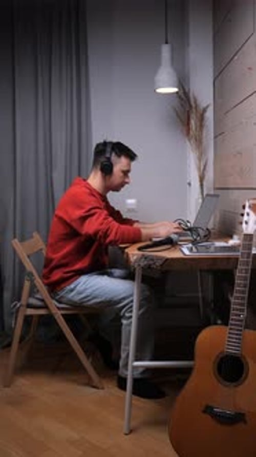 Man Works at Desk with Laptop and Guitar