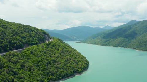 Stunning aerial establishing shot of mountain valley turquoise lake surrounded by lush forest. Road