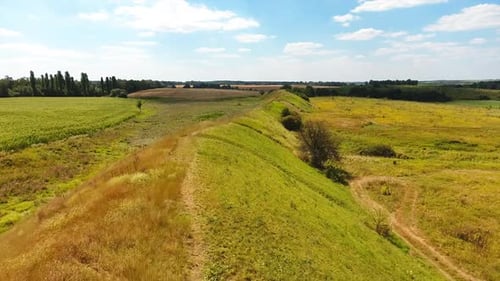 Summer green landscape under blue skies. Long hill separating meadows from agricultural farmlands.