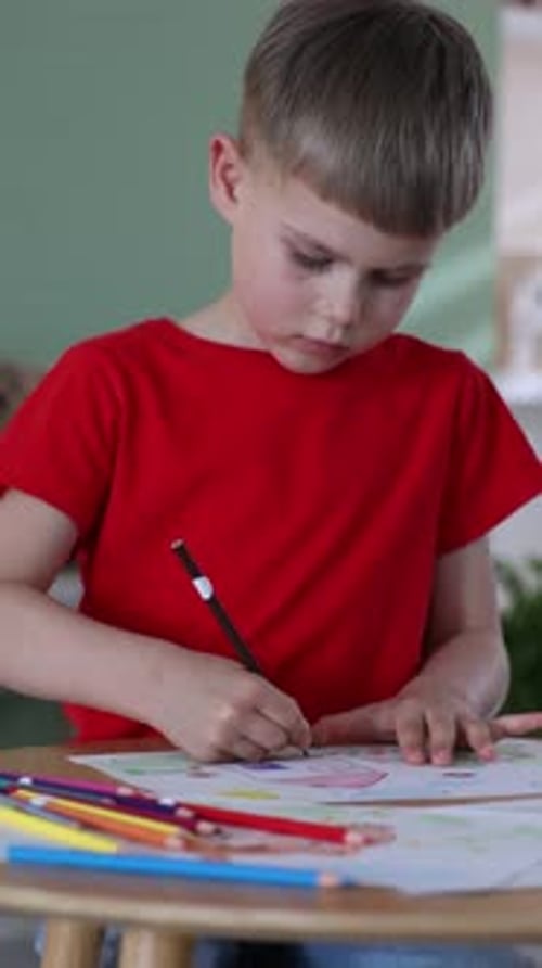 Kleiner Junge zeichnet ein Bild mit Bleistift auf einem Holzschreibtisch im Haus