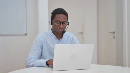 Man with Headset Typing on Laptop in Office