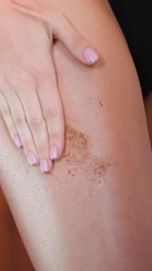 Woman's Hand Applying Exfoliating Scrub To Leg