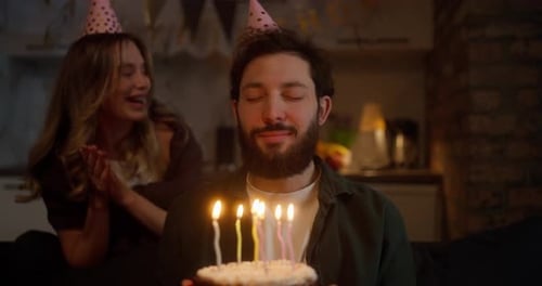 Happy Guy in Birthday Cap Blowing Out Candles on Cake During Birthday Party with His Girlfriend at