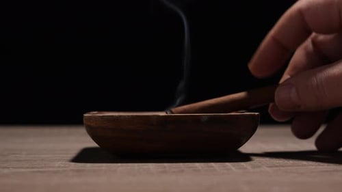 Hand Placing Cigar in Ashtray with Rising Smoke