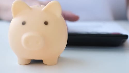 Close Up Piggy Bank with Female Hand Counting on Calculator on Background