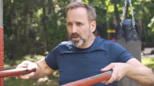 Ein gutaussehender kaukasischer Mann mittleren Alters macht eine einfache Variation von Körpergewichtsreihen mit Dip Bars