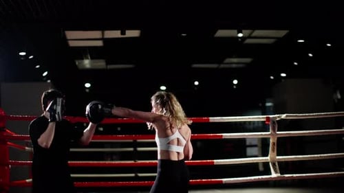 Woman Practicing Boxing in Gym with a Male Trainer Preparing to Throw a Punch While Wearing Black
