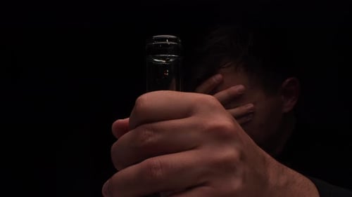 Troubled Man Holding Bottle of Alcohol in Dark Room