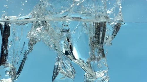 Ice cubes falling into water, splashing against blue