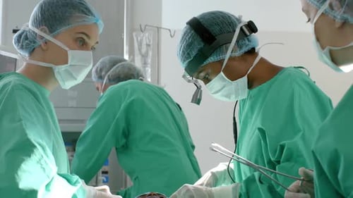 Diverse surgeons wearing surgical gowns operating on patient in operating theatre, slow motion